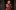 A Doll's House PT2-2019-13 A white woman with strawberry blonde hair in an up-do, wearing a red and black 19th-century city suit, stands pointing her finger at someone out of the frame.