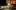 Frog Princess-2019-8 A white woman in a frog costume sits as she pours various ingredients into a gold mixing bowl. There is an air of comedy and farce.