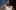 1476194_10152019483045502_1014006748_n A Black woman with black hair is in a white dress, standing with her arms on her hips. Behind her is a white patterned wall.
